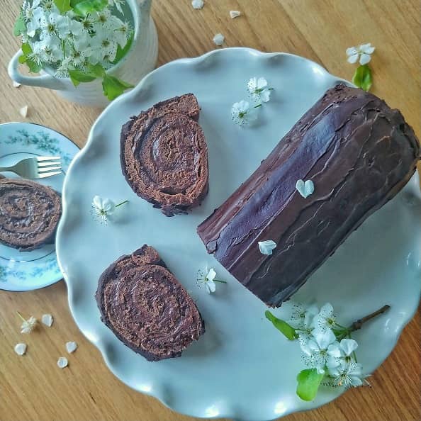 Chocolate Swiss Roll on a table with floral arrangement.
