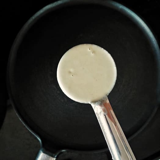 Non stick pan and dosa batter in a spoon.